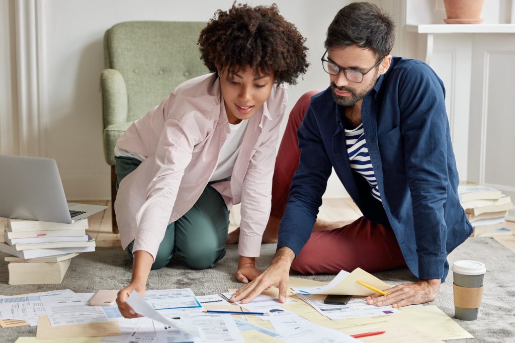 Horizontal shot of multiethnic investors study investment portfolio together, surrounded with paper