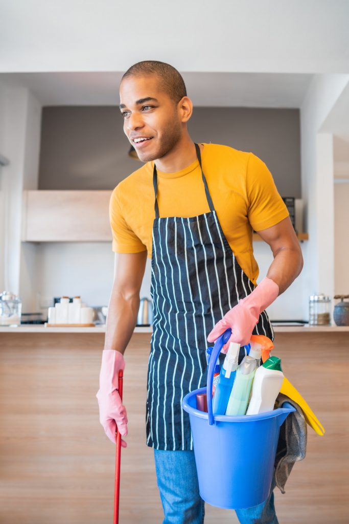Latin man holding a bucket with cleaning items.